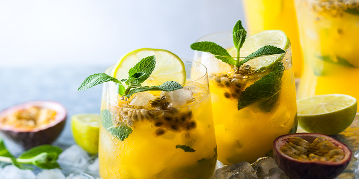 Copo cheio de suco de maracujá com folhas de hortelã e limão